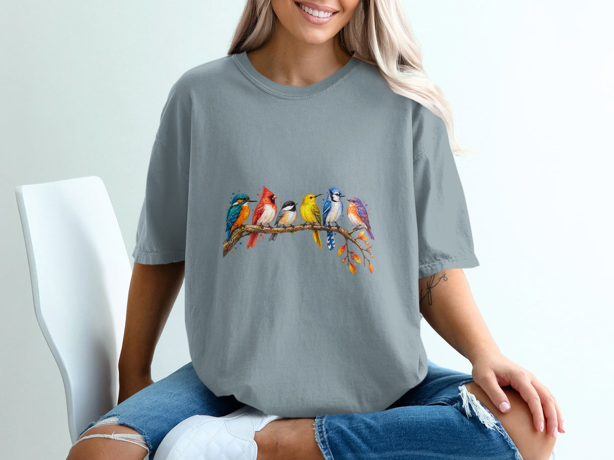 Watercolor art of six colorful birds perched on a branch on a gray t-shirt.