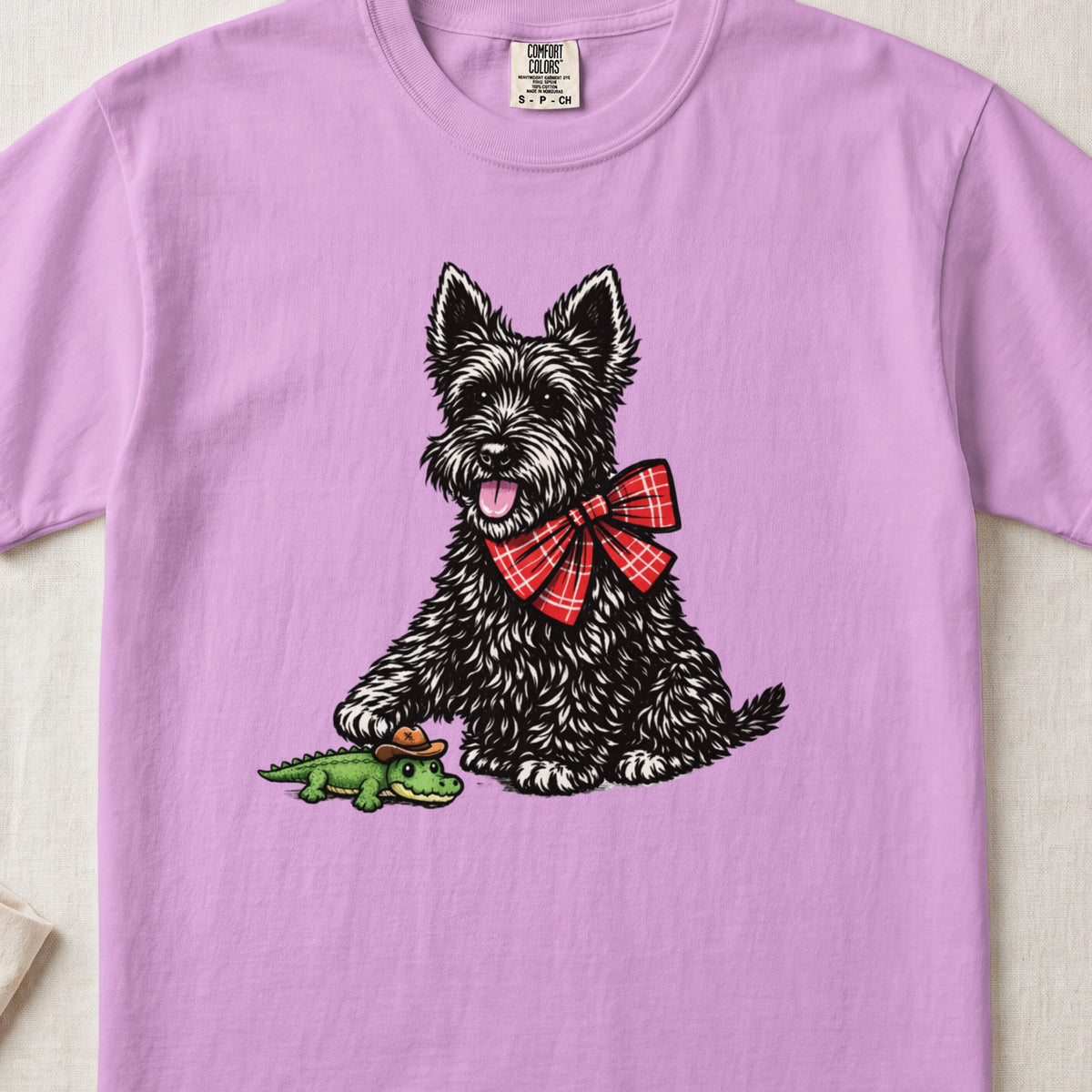 A light purple t-shirt featuring a graphic of a black terrier wearing a red plaid bow.
