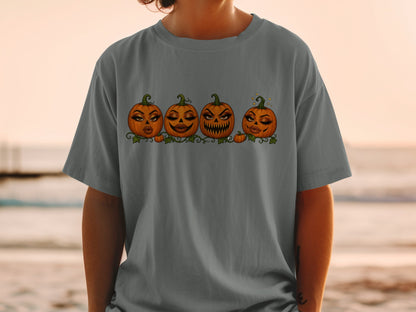 Four cartoon pumpkins with makeup and varying facial expressions, printed on a gray t-shirt.
