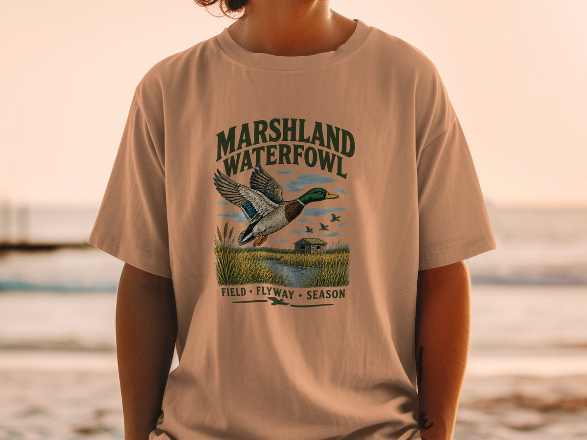 T-shirt graphic of a mallard duck in flight over a marsh with a cabin and text.