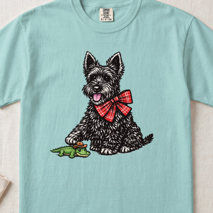 Light blue t-shirt featuring an illustration of a black terrier wearing a red plaid bow tie and touching a toy alligator.