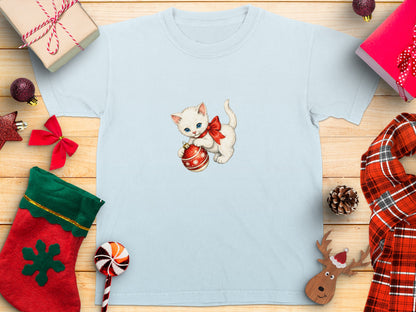 Light blue t-shirt with a white kitten wearing a red bow holding a Christmas ornament.