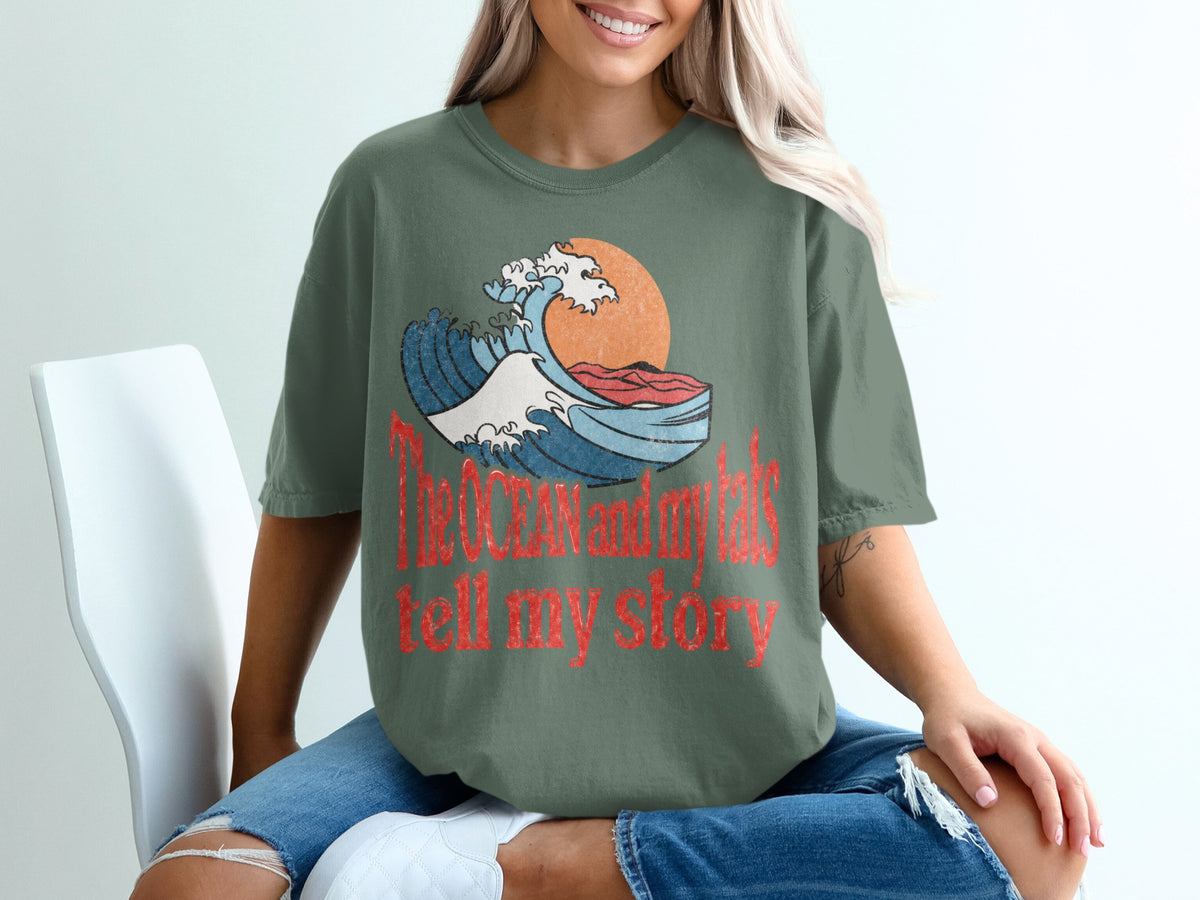 Green t-shirt with graphic of a wave, sun, and text: "The ocean and my tats tell my story".
