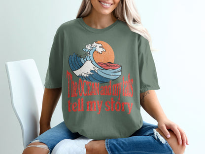 Green t-shirt with graphic of a wave, sun, and text: "The ocean and my tats tell my story".