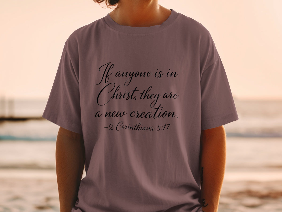 Mauve t-shirt with "If anyone is in Christ, they are a new creation. -2 Corinthians 5:17" in script font.