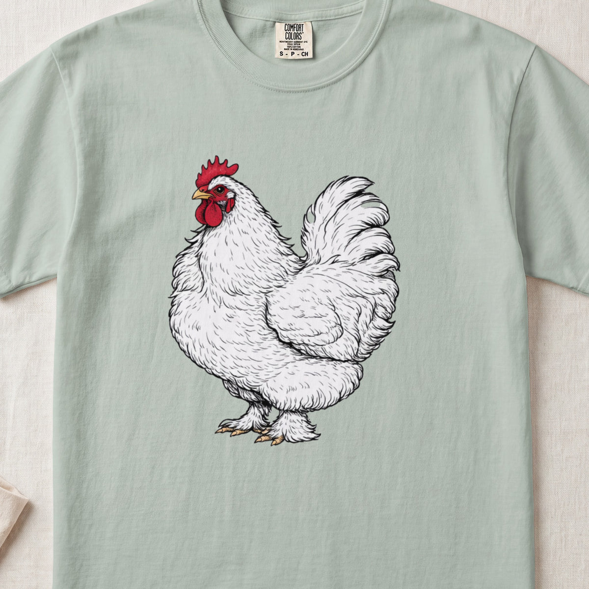 Sage green t-shirt featuring a detailed black and white illustration of a white rooster with a red comb.