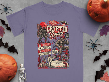 Purple t-shirt with "Cryptid Rodeo" graphic featuring Bigfoot, Mothman, and other cryptids.