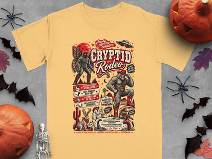 Yellow t-shirt with Cryptid Rodeo graphic featuring Bigfoot, Mothman, and UFO.