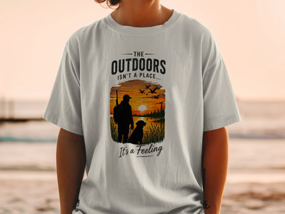T-shirt graphic with hunter, dog, sunset, and text "The Outdoors Isn't a Place... It's a Feeling."