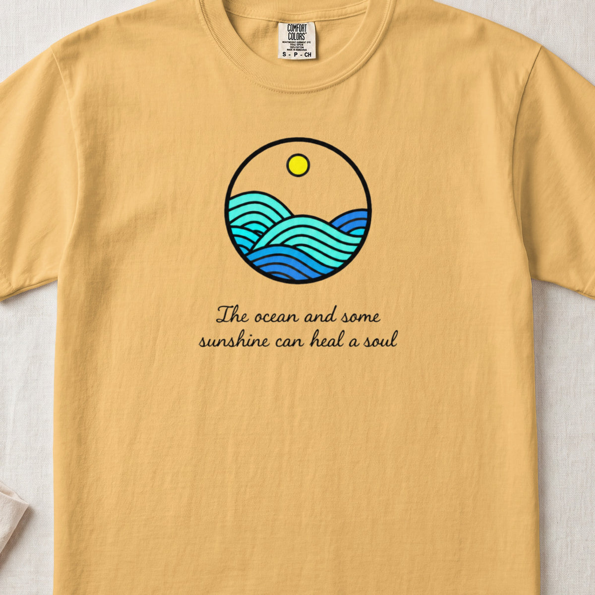 A yellow t-shirt features a circular ocean graphic with a sun and the text "The ocean and some sunshine can heal a soul".