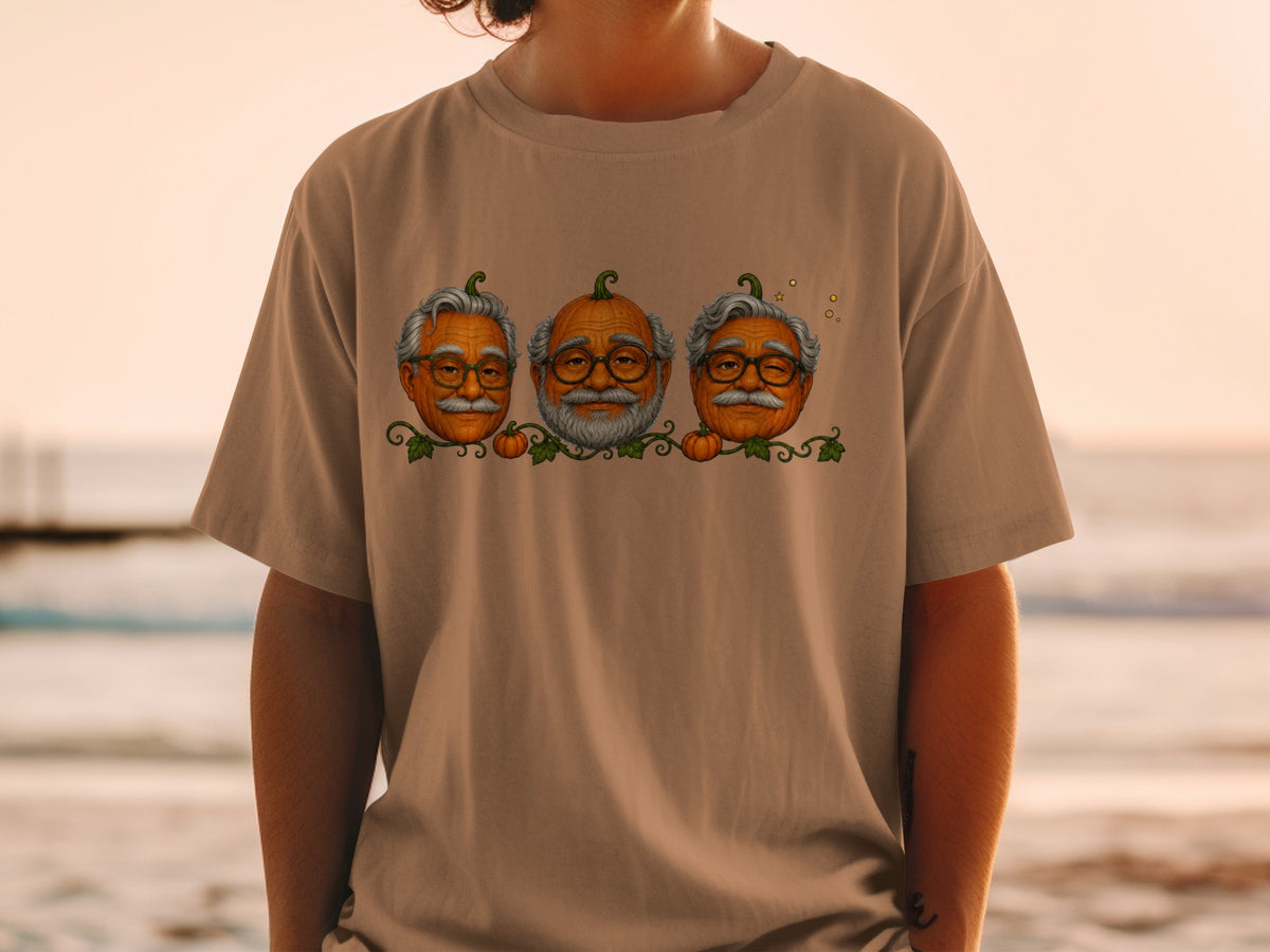 Three pumpkins with human faces and glasses on a brown t-shirt.
