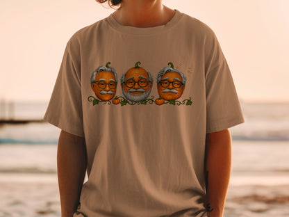 Three pumpkins with human faces and glasses on a brown t-shirt.