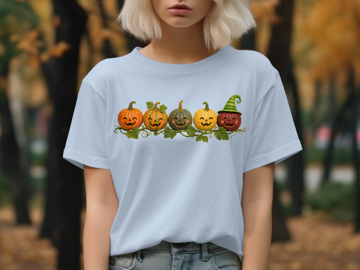Light blue t-shirt with a row of five smiling pumpkins, one wearing a green striped hat.