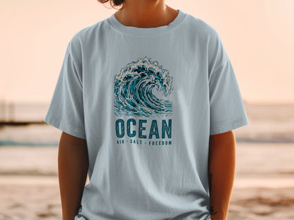 Light blue t-shirt with a graphic of a breaking wave and the text "OCEAN AIR SALT FREEDOM".