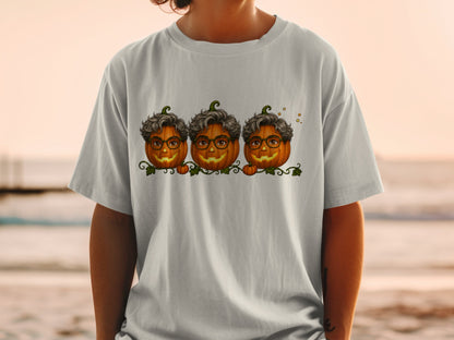 Three smiling pumpkins with glasses and curly hair on a shirt.