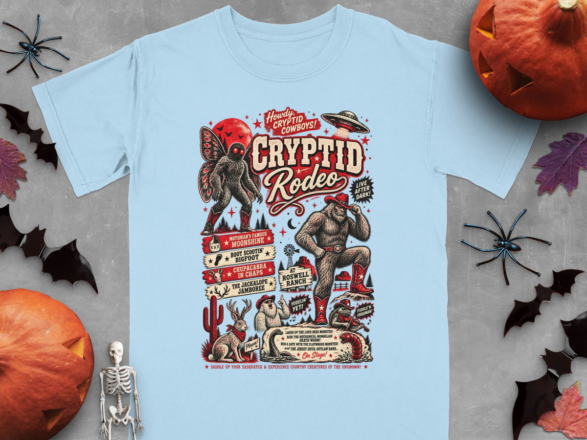 Light blue t-shirt with Cryptid Rodeo graphic featuring Mothman, Bigfoot, UFO, and other creatures.