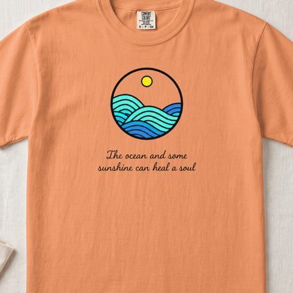 An orange t-shirt featuring a circular ocean wave illustration and text that reads The ocean and some sunshine can heal a soul.