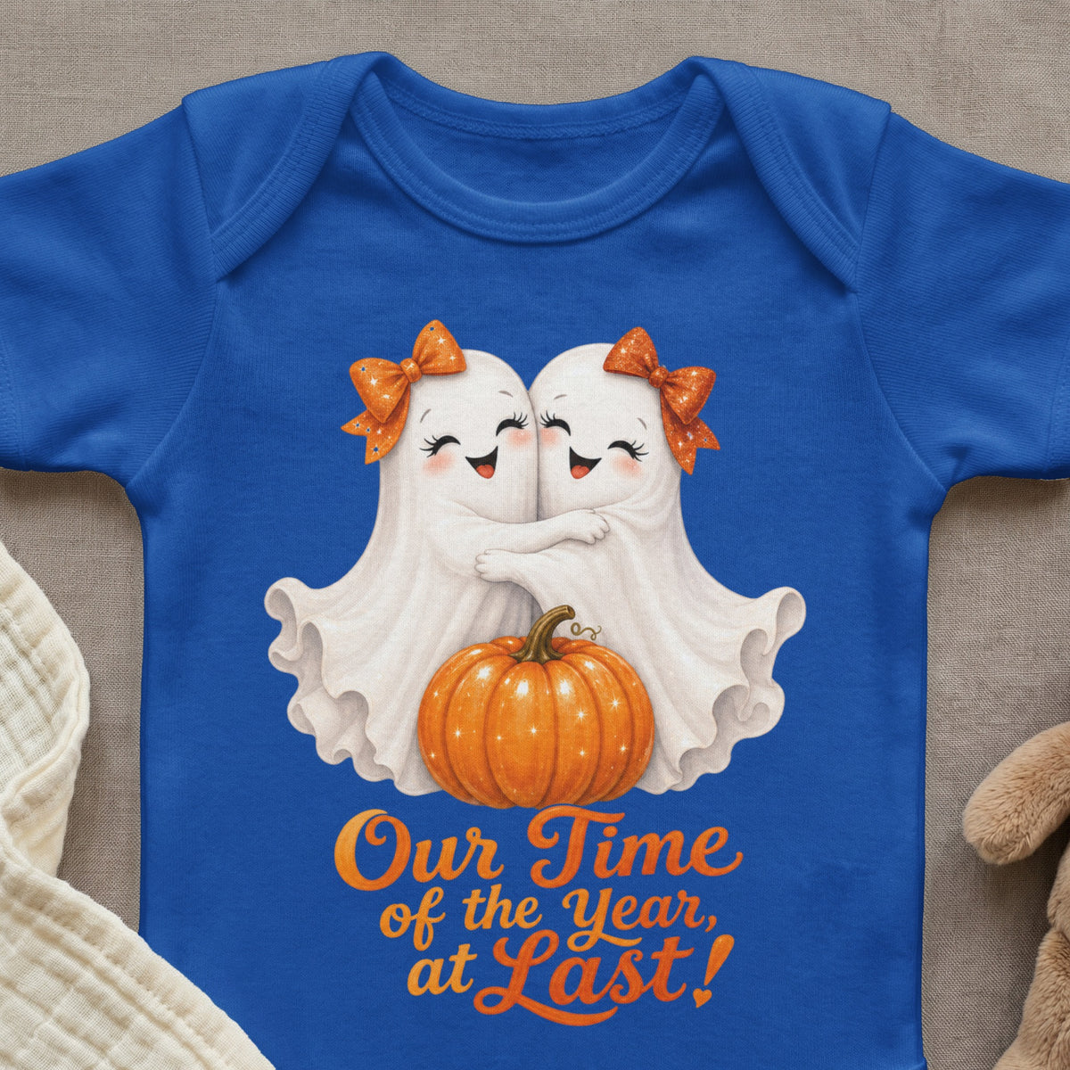Two cartoon ghosts hug beside a pumpkin on a blue bodysuit with text.