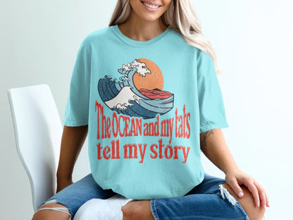 Light blue t-shirt with wave graphic and text "The OCEAN and my tats tell my story".