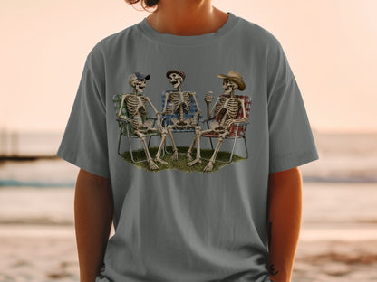 Three skeletons sit in lawn chairs with drinks, wearing hats.