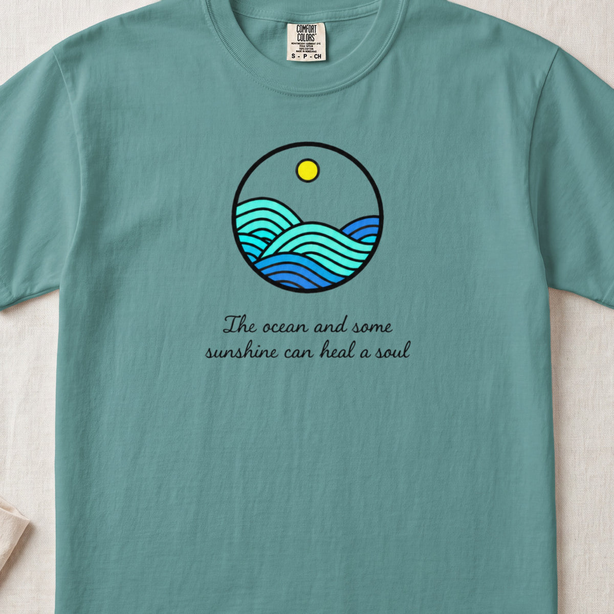 Teal t-shirt featuring a circular ocean graphic and the text The ocean and some sunshine can heal a soul.
