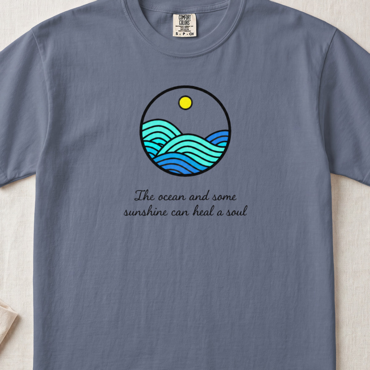 A blue crew neck t-shirt featuring a circular graphic of waves and text reading The ocean and some sunshine can heal a soul.