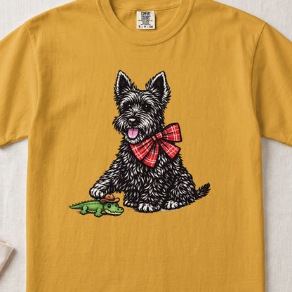 Gold t-shirt featuring an illustration of a black Scottish Terrier wearing a red plaid bow tie next to a small alligator toy.