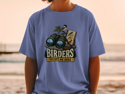 Binoculars, notebook, and birds graphic on a purple t-shirt with "Birders You Got Me Here" text.