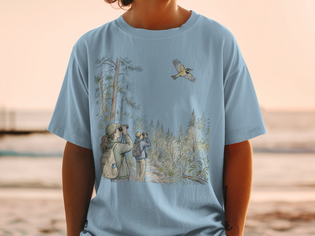 Light blue t-shirt with a watercolor-style illustration of birdwatchers in a forest with a flying bird.