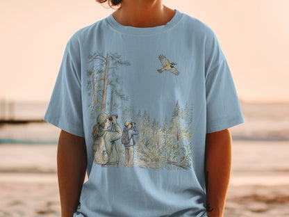 Light blue t-shirt with a watercolor-style illustration of birdwatchers in a forest with a flying bird.