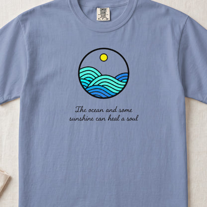 A blue t-shirt featuring a circular graphic of ocean waves and the text The ocean and some sunshine can heal a soul.