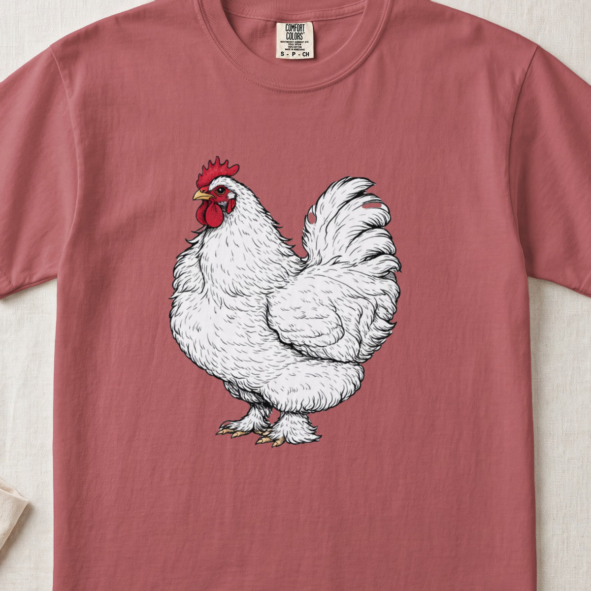 A vintage-style graphic of a fluffy white rooster centered on a dusty red t-shirt.