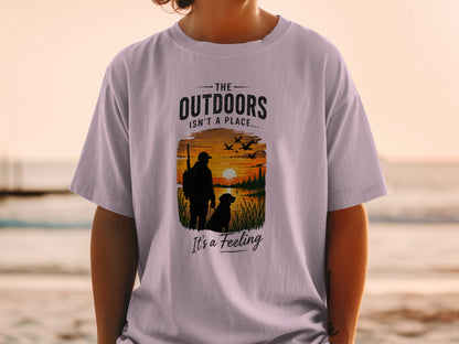 T-shirt graphic: Hunter with dog, sunset, and text "The Outdoors Isn't A Place... It's A Feeling".
