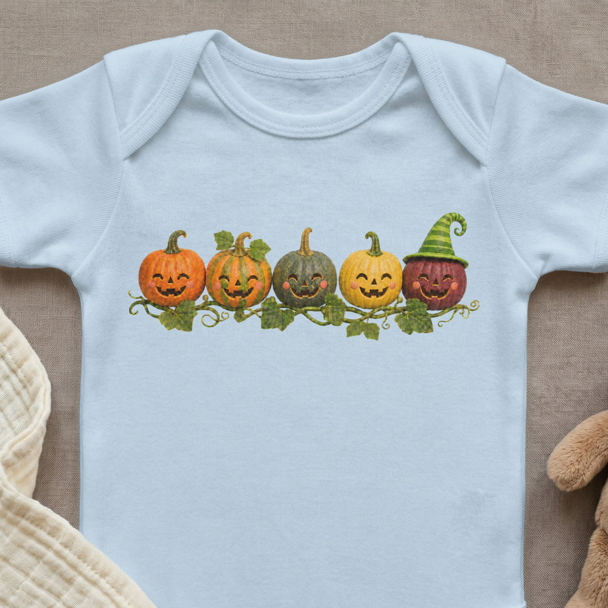 Light blue baby onesie with line of five smiling jack-o'-lanterns and green striped hat.