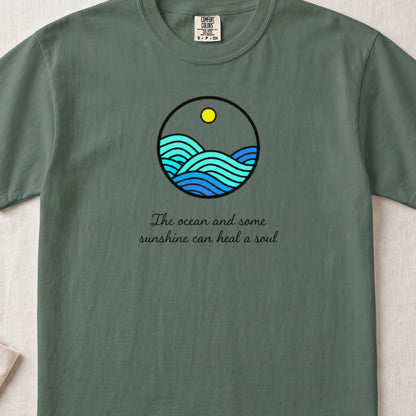 Olive green t-shirt with a round graphic of ocean waves, a sun, and the text The ocean and some sunshine can heal a soul.