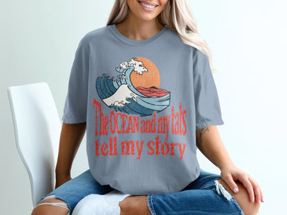 T-shirt with text "The ocean and my tats tell my story" and wave graphic.