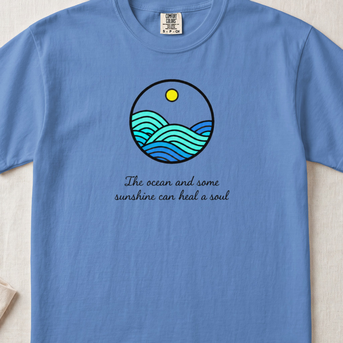 A blue t-shirt featuring a circular ocean graphic with text reading The ocean and some sunshine can heal a soul.