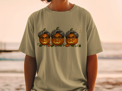 Three pumpkins with glasses and curly hair wear a vine design on a tan shirt.