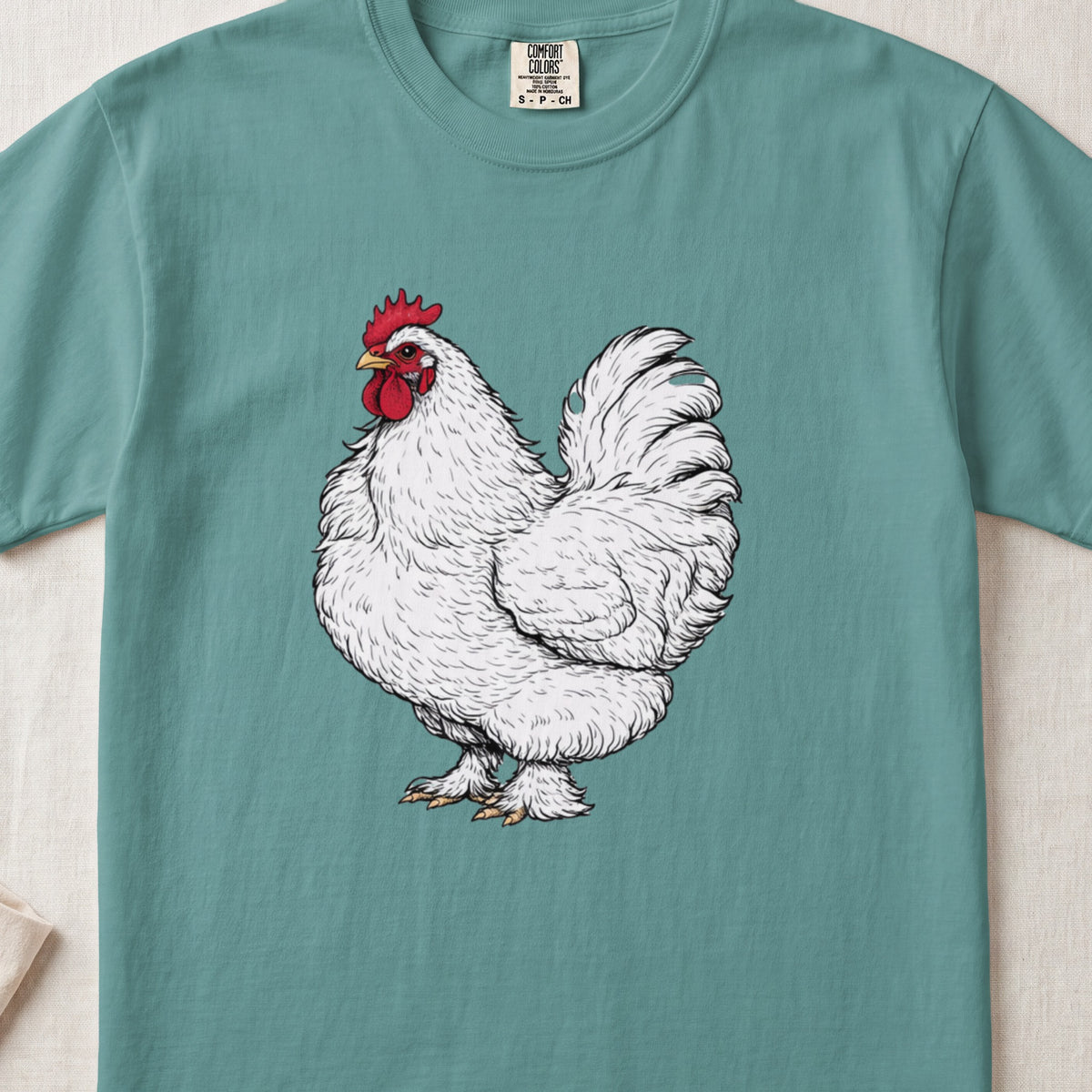 A teal crewneck t-shirt featuring a detailed illustration of a white rooster centered on the chest.