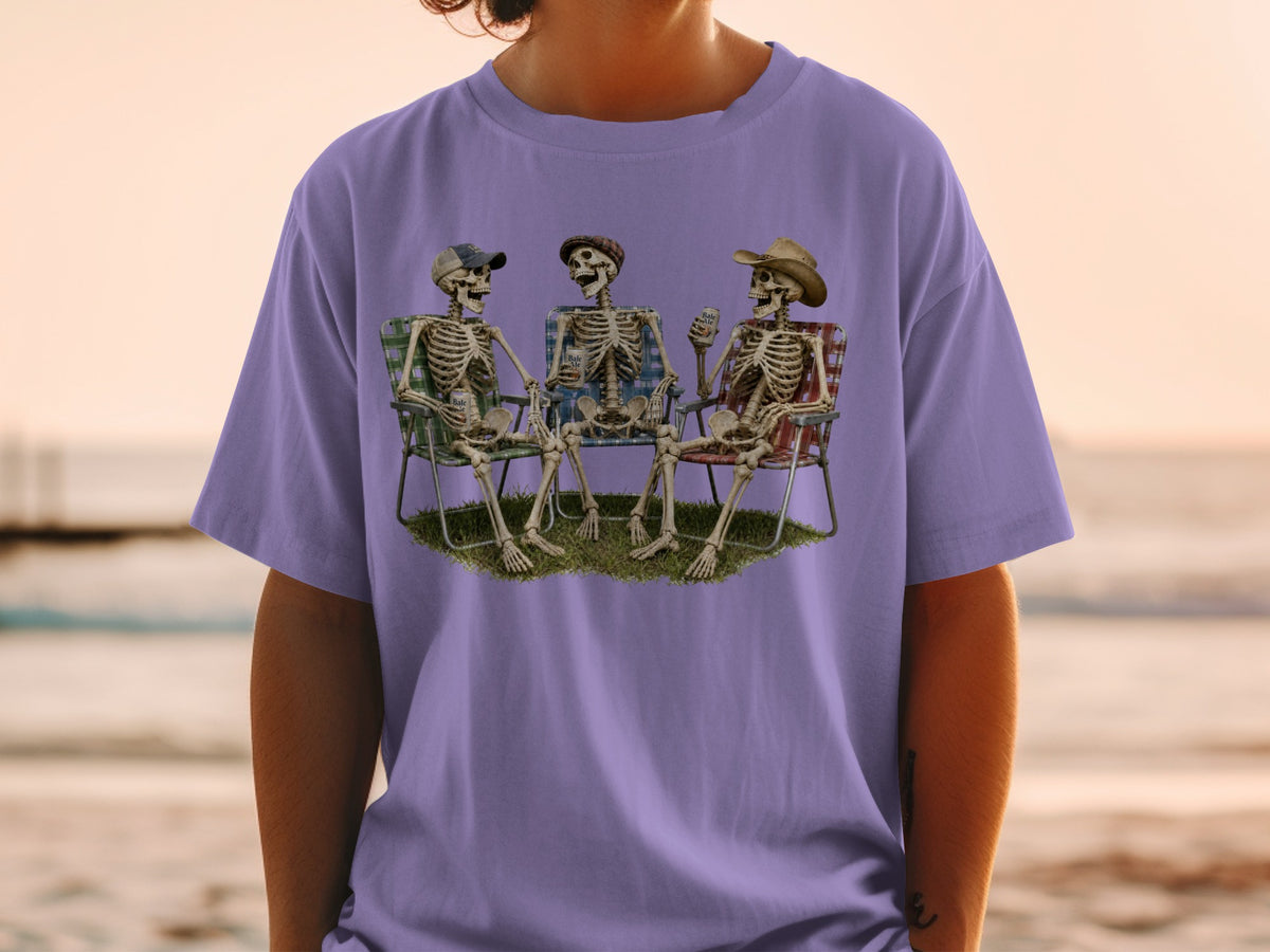 Three skeletons sitting in chairs on grass, two holding cans of beer.
