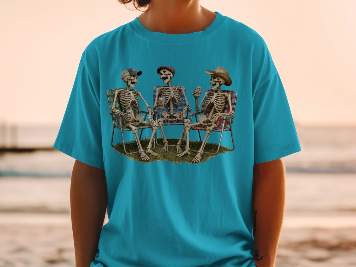 Three skeletons sit on lawn chairs on the beach, holding drinks.