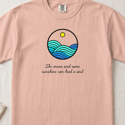Pink t-shirt with a circular graphic of blue ocean waves, a sun, and the text The ocean and some sunshine can heal a soul.