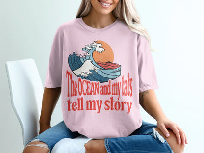 Pink t-shirt with distressed print of wave, sun, and text "The OCEAN and my tats tell my story".