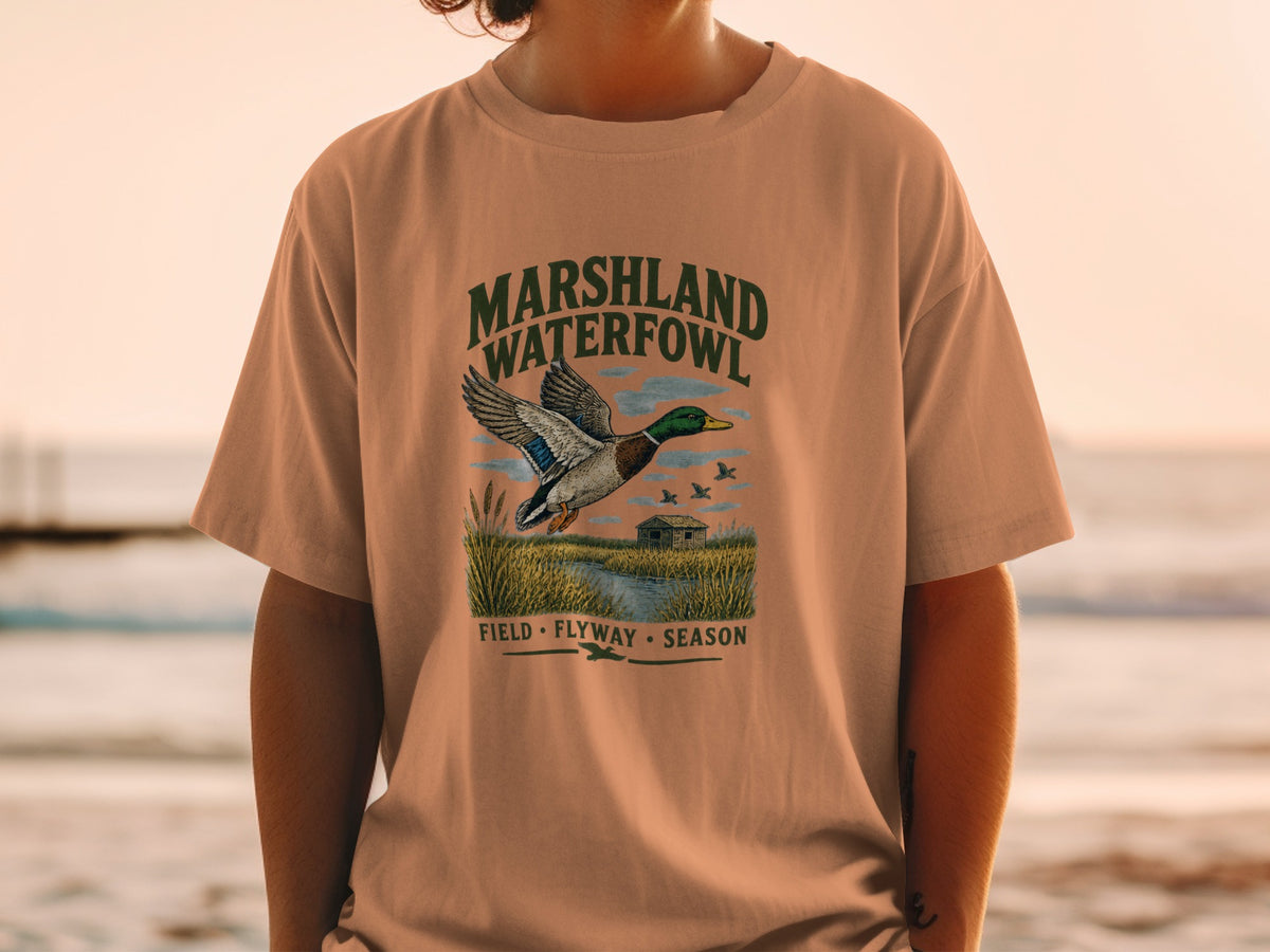 T-shirt graphic with mallard duck flying over marshland, "MARSHLAND WATERFOWL" text.