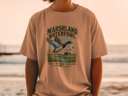 T-shirt graphic with mallard duck flying over marshland, "MARSHLAND WATERFOWL" text.