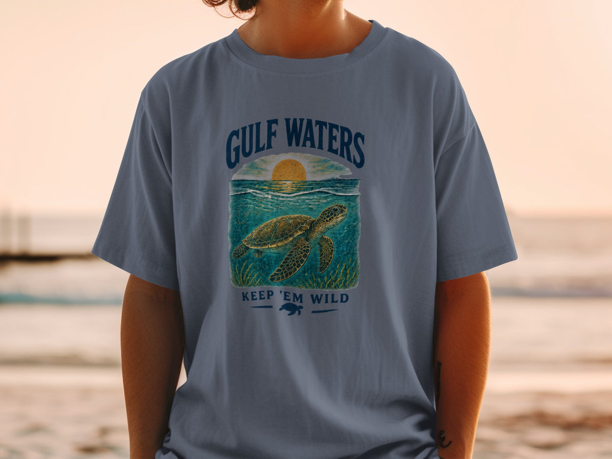 Blue t-shirt with "Gulf Waters" text and a sea turtle swimming at sunset graphic.