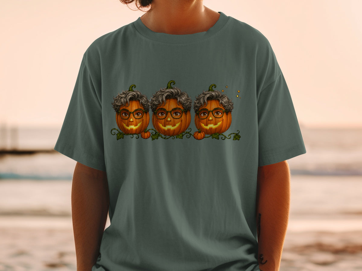 Three smiling jack-o'-lanterns with glasses and curly hair on a dark green t-shirt.