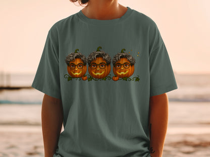 Three smiling jack-o'-lanterns with glasses and curly hair on a dark green t-shirt.