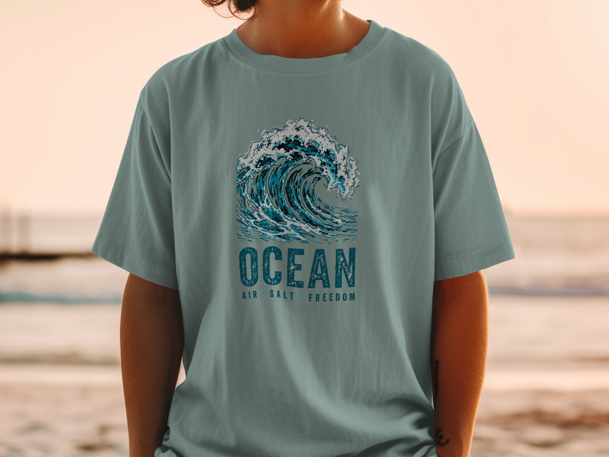 Blue wave graphic with "OCEAN AIR SALT FREEDOM" text on a teal t-shirt.