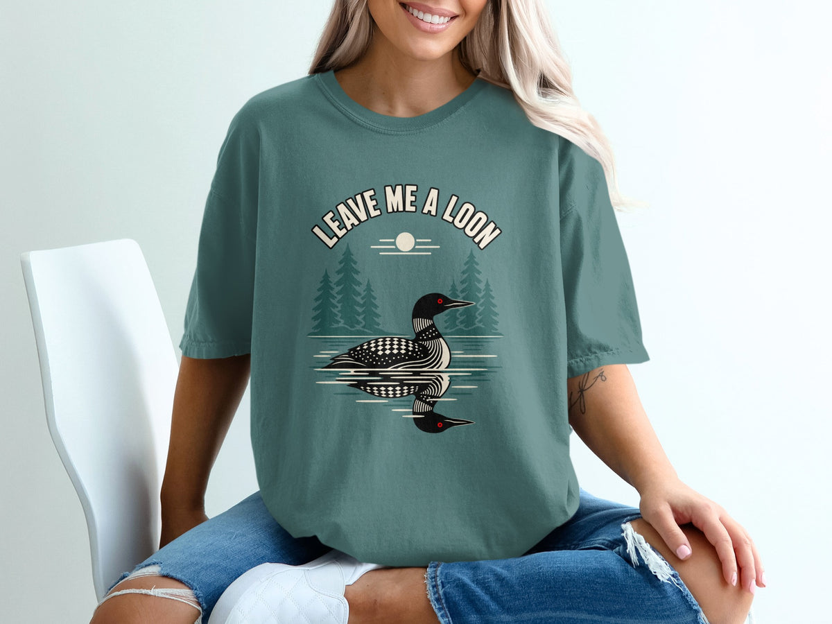Green t-shirt with a loon and trees graphic and "Leave Me A Loon" text.